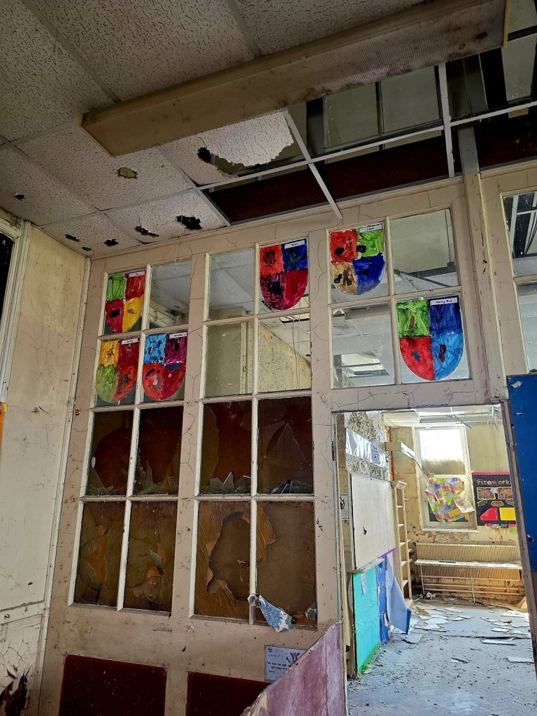 Colourful painted shields in the upper glazing of a school partition with smashed lower panes