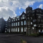 Exterior of the abandoned former Manselton School in Swansea, a three-storey Victorian stone building with turrets, boarded ground-floor windows and weeds growing through the yard