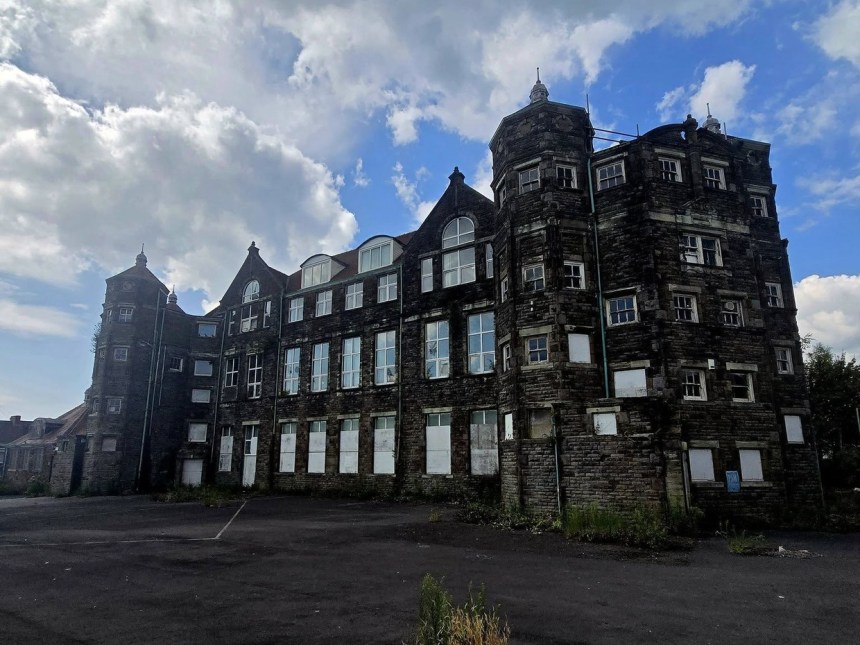 Exterior of the abandoned former Manselton School in Swansea, a three-storey Victorian stone building with boarded windows