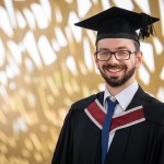 Jonathan Phillips in cap and gown smiling outside Swansea University's Bay Campus
