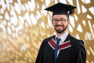 Jonathan Phillips in cap and gown smiling outside Swansea University's Bay Campus