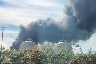 Black smoke billows behind large white spherical gas storage tanks at the Impala terminal in Milford Haven.