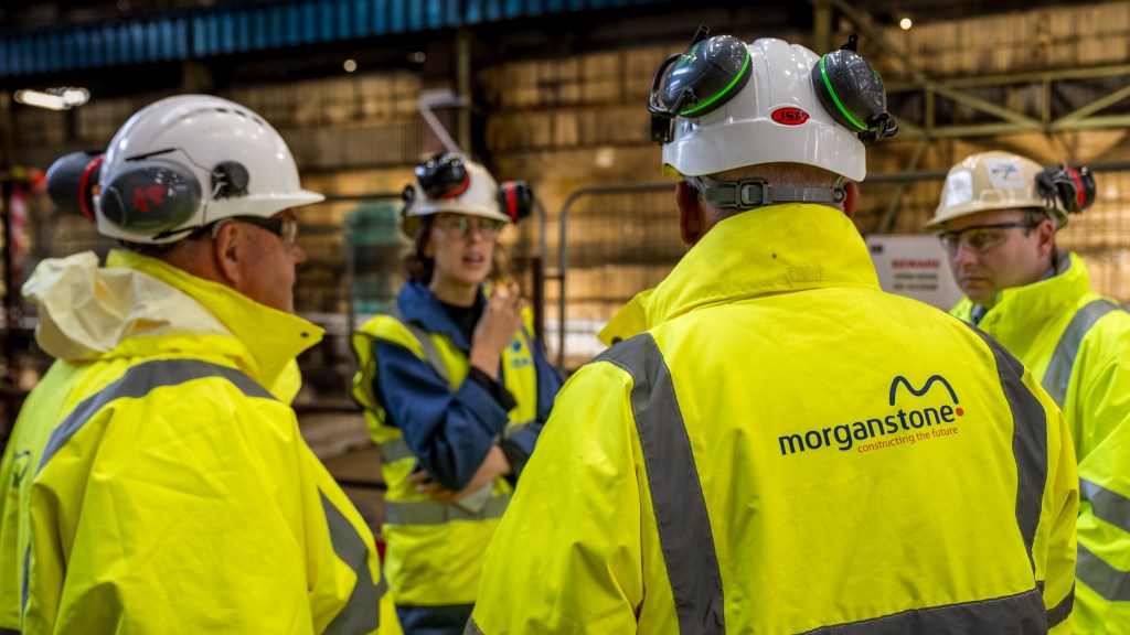 Four people in hi-vis and hard hats in conversation inside the steelworks, one wearing a Morganstone jacket