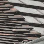 A roof with rows of dark tiles sitting unevenly and out of line, with visible gaps between courses.