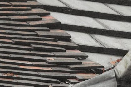 A roof with rows of dark tiles sitting unevenly and out of line, with visible gaps between courses.