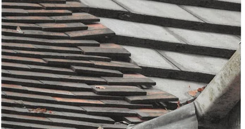 A roof with rows of dark tiles sitting unevenly and out of line, with visible gaps between courses.