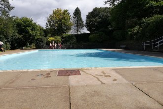 The filled paddling pool at Parc Howard, Llanelli, surrounded by trees with families sitting at the poolside