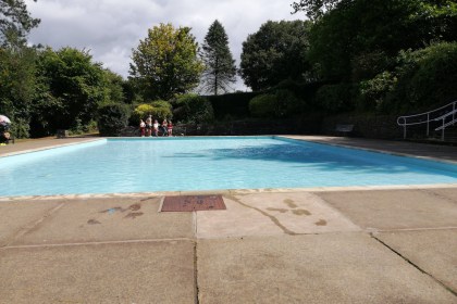 The filled paddling pool at Parc Howard, Llanelli, surrounded by trees with families sitting at the poolside