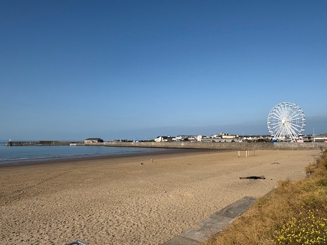 A wide view of Sandy Bay beach in Porthcawl on a sunny day, with the new white big wheel rising above the seafront in the distance