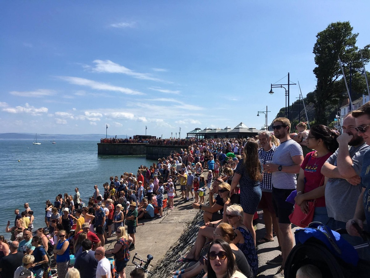 Homemade rafts crossing the water off Mumbles with crowds on the sea wall and Oystermouth Castle on the hillside behind