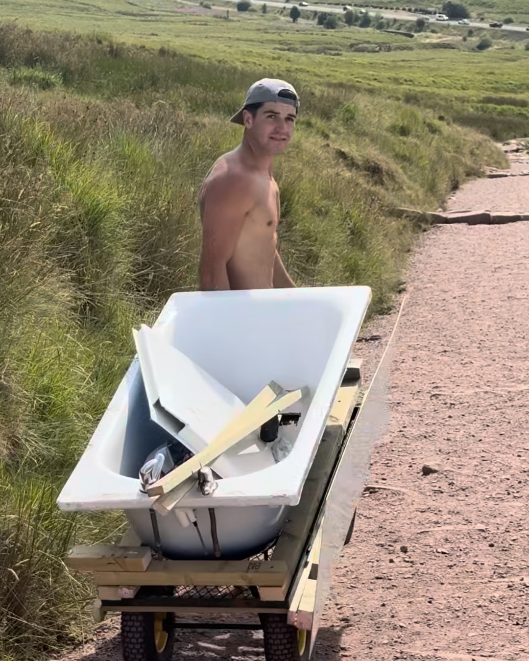 A white bath on a wheeled wooden frame loaded with broken panels and lengths of timber.