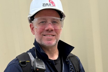 Shaun Young in a white Zulu Joint Integrity hard hat, safety glasses and navy overalls, smiling on an industrial site