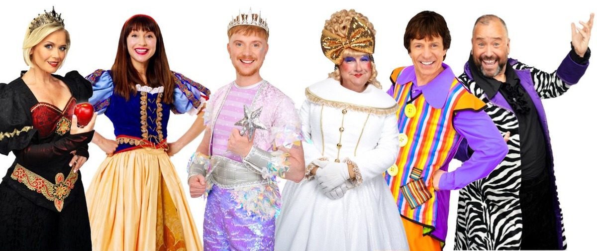 Six pantomime cast members in costume against a white background — the Wicked Queen in a black gown holding a red apple, Snow White in a blue and gold dress, the Spirit of the Forest in a silver crown, a dame in a white sequinned gown and gold bow, a comic in a striped waistcoat, and a henchman in a zebra-print coat.