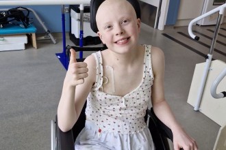 Soffia smiling and giving a thumbs up from her wheelchair in a hospital rehabilitation room
