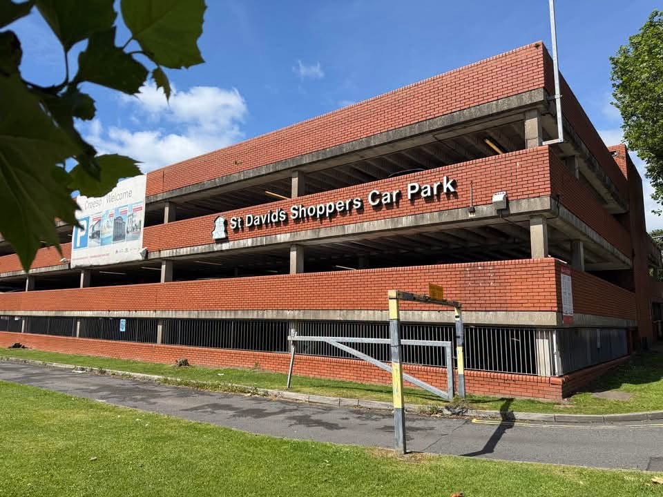 The red-brick St Davids Shoppers Car Park multi-storey with its name in white lettering, seen from a grass verge