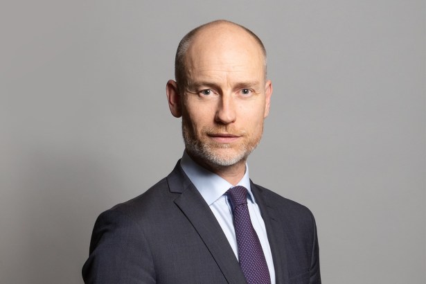 Official parliamentary portrait of Stephen Kinnock MP, wearing a dark suit and purple tie against a grey background