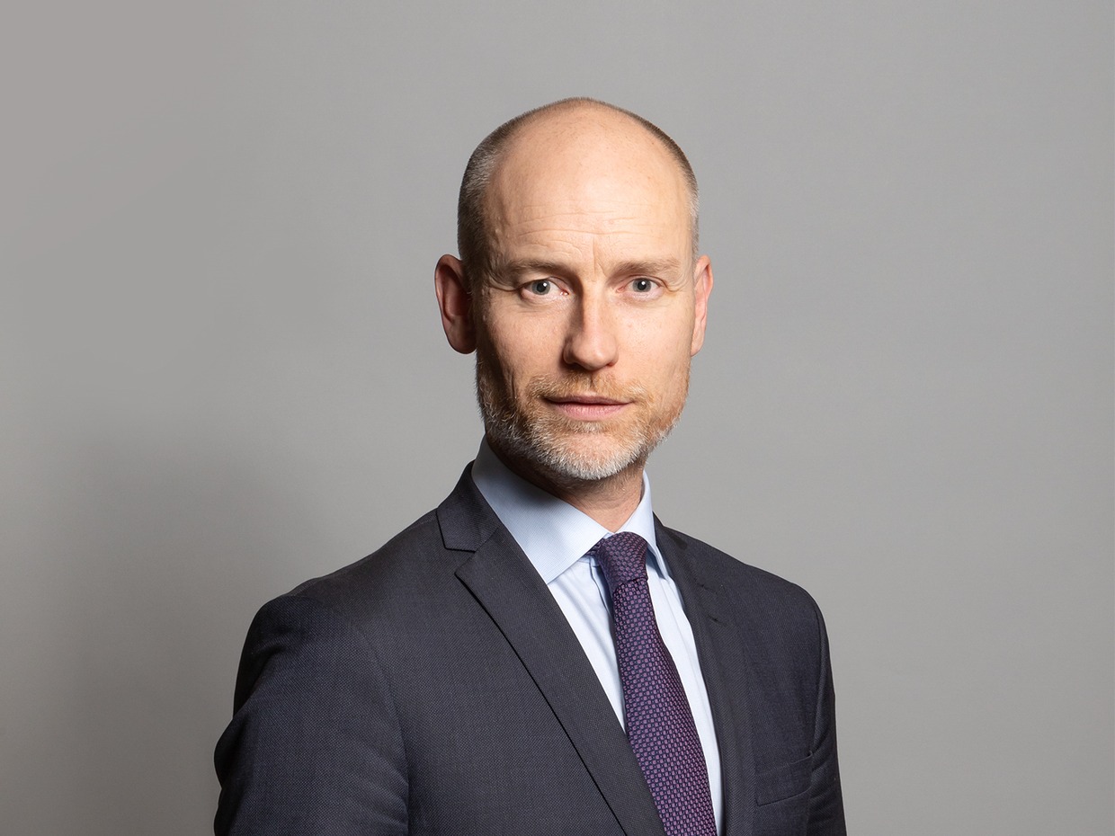 Official parliamentary portrait of Stephen Kinnock MP, wearing a dark suit and purple tie against a grey background
