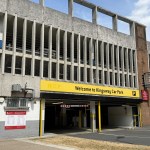The multi-storey Kingsway car park with a yellow NCP Welcome to Kingsway Car Park sign above the entrance and a red Swansea Council sign and tariff board on the wall below