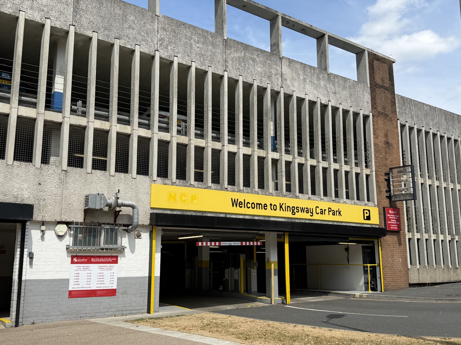 The multi-storey Kingsway car park with a yellow NCP Welcome to Kingsway Car Park sign above the entrance and a red Swansea Council sign and tariff board on the wall below