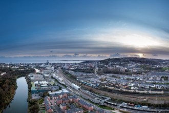 Aerial view of Swansea city centre at dusk, with the River Tawe, railway lines into High Street station, new riverside housing and Kilvey Hill