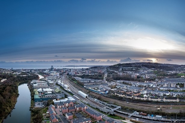 Aerial view of Swansea city centre at dusk, with the River Tawe, railway lines into High Street station, new riverside housing and Kilvey Hill