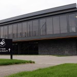 The exterior of Swansea City's first team training facility at Fairwood, a modern glass-fronted building with the club crest on a sign outside.