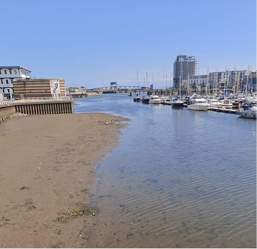 A large exposed sandbank beside shallow water in the River Tawe basin, with yachts moored at Swansea Marina