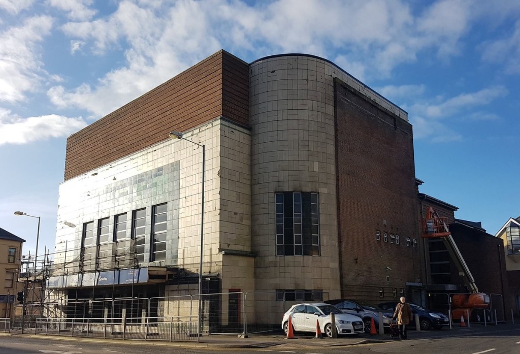 The former Odeon cinema in Llanelli, a large Art Deco building with a curved white-tiled tower, surrounded by security fencing and scaffolding.