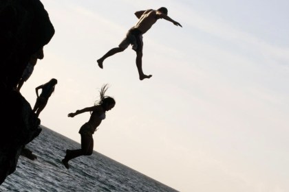 Silhouettes of two people jumping from a rocky cliff into the sea, with others watching from the rocks (stock image — not the incident described in the article)