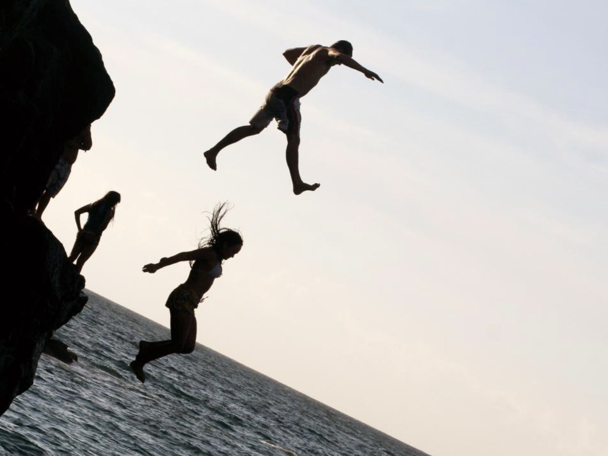 Silhouettes of two people jumping from a rocky cliff into the sea, with others watching from the rocks (stock image — not the incident described in the article)