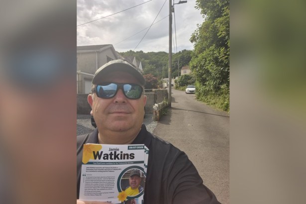 Jamie Watkins in sunglasses and a cap takes a selfie on a Trebanos street holding a bundle of his Plaid Cymru campaign leaflets