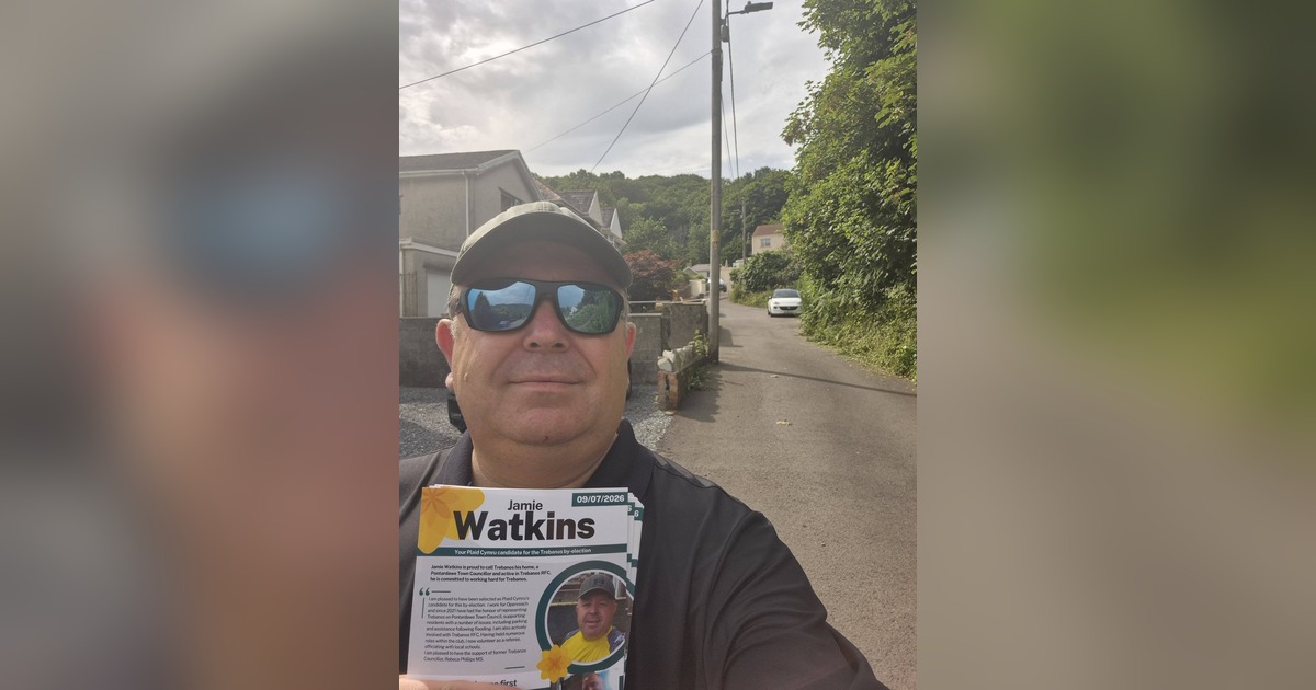 Jamie Watkins in sunglasses and a cap takes a selfie on a Trebanos street holding a bundle of his Plaid Cymru campaign leaflets