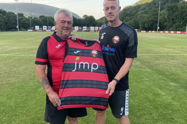 Two men hold up a red-and-black hooped Trefelin BGC shirt on the pitch at Ynys Park