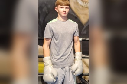 Tyler Ford, an 18-year-old with short light brown hair, standing in a boxing gym wearing grey boxing gloves.