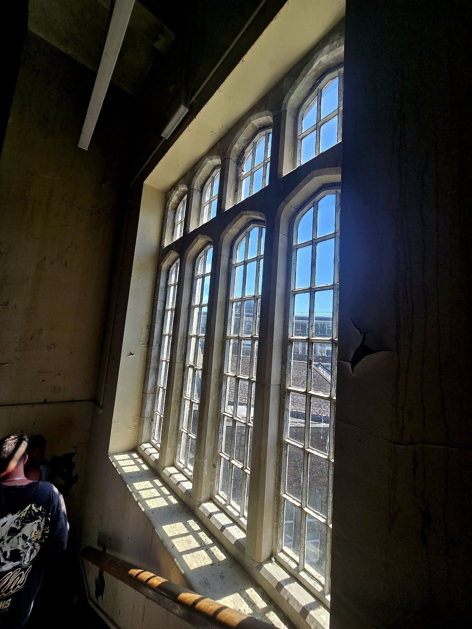 Tall arched leaded windows casting sunlight into a dark stairwell