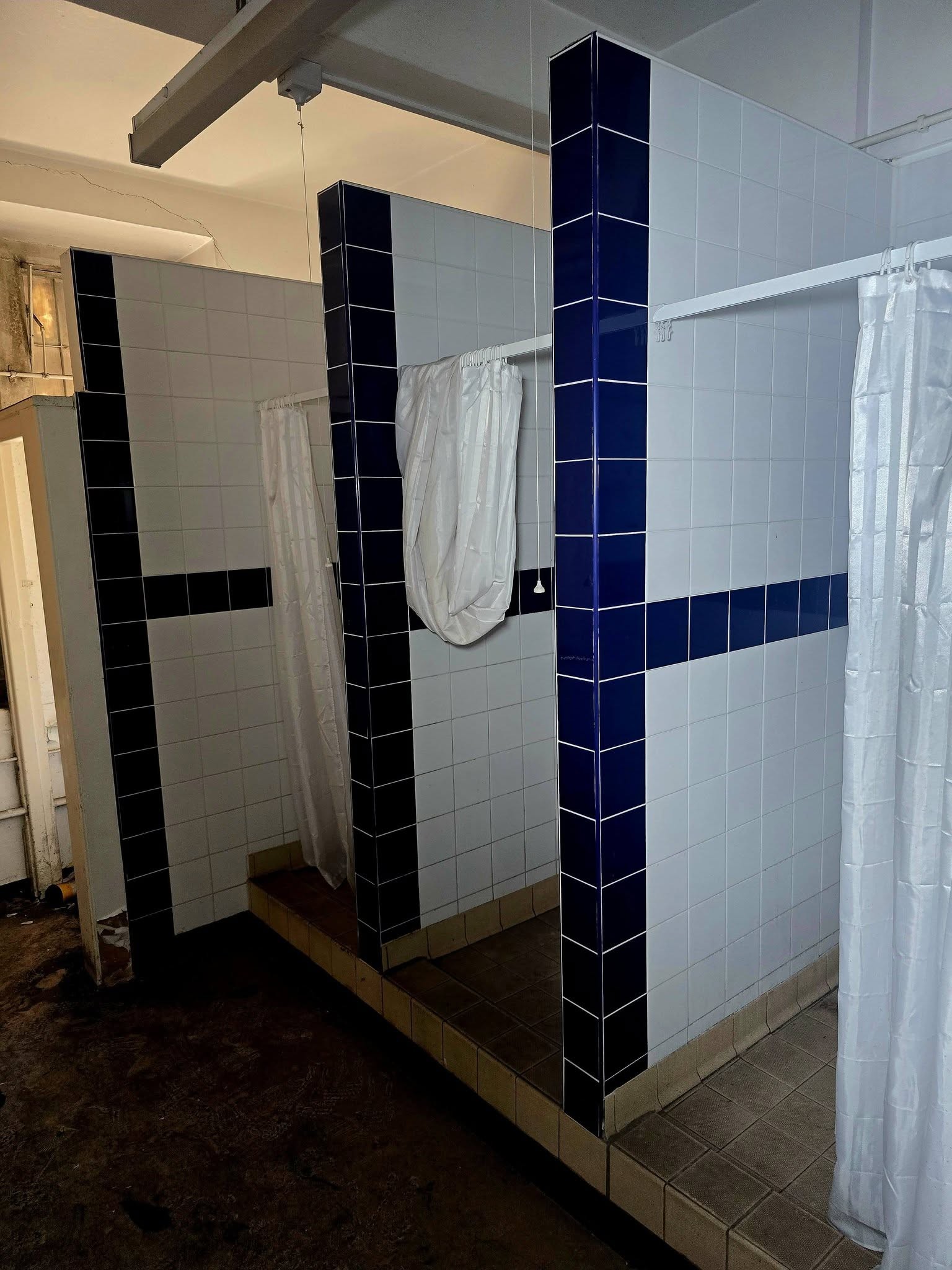 Blue and white tiled shower cubicles with curtains still hanging