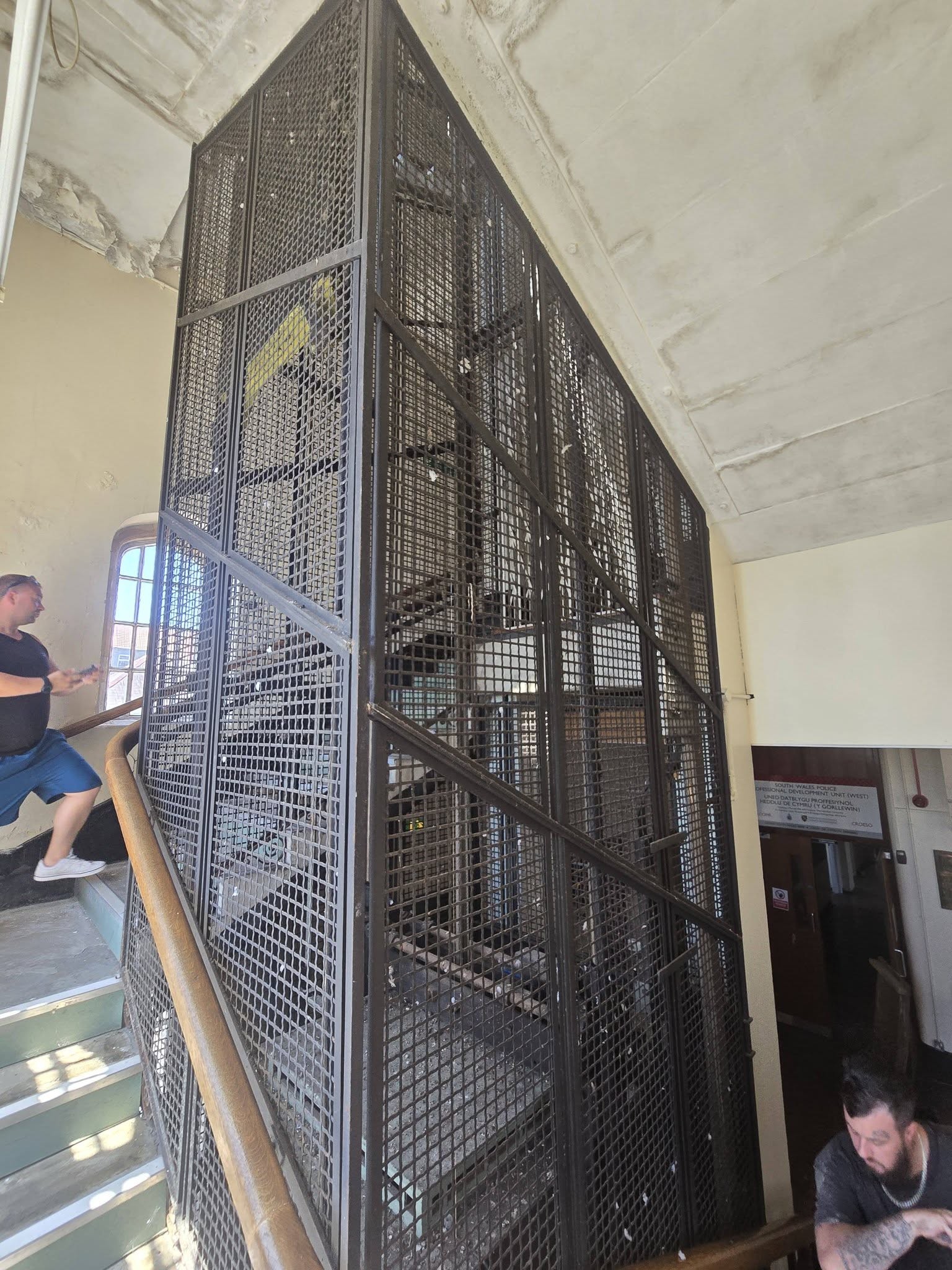 Black mesh caged lift shaft rising through a stone staircase