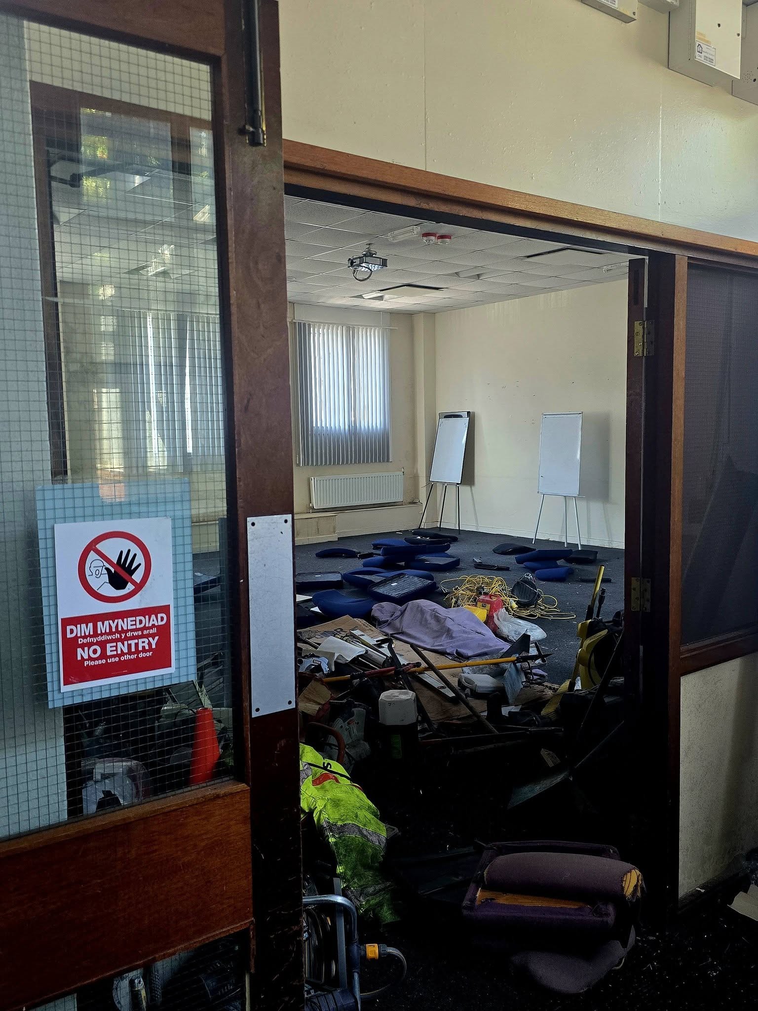 Vandalised training room seen through a door with a bilingual no entry sign