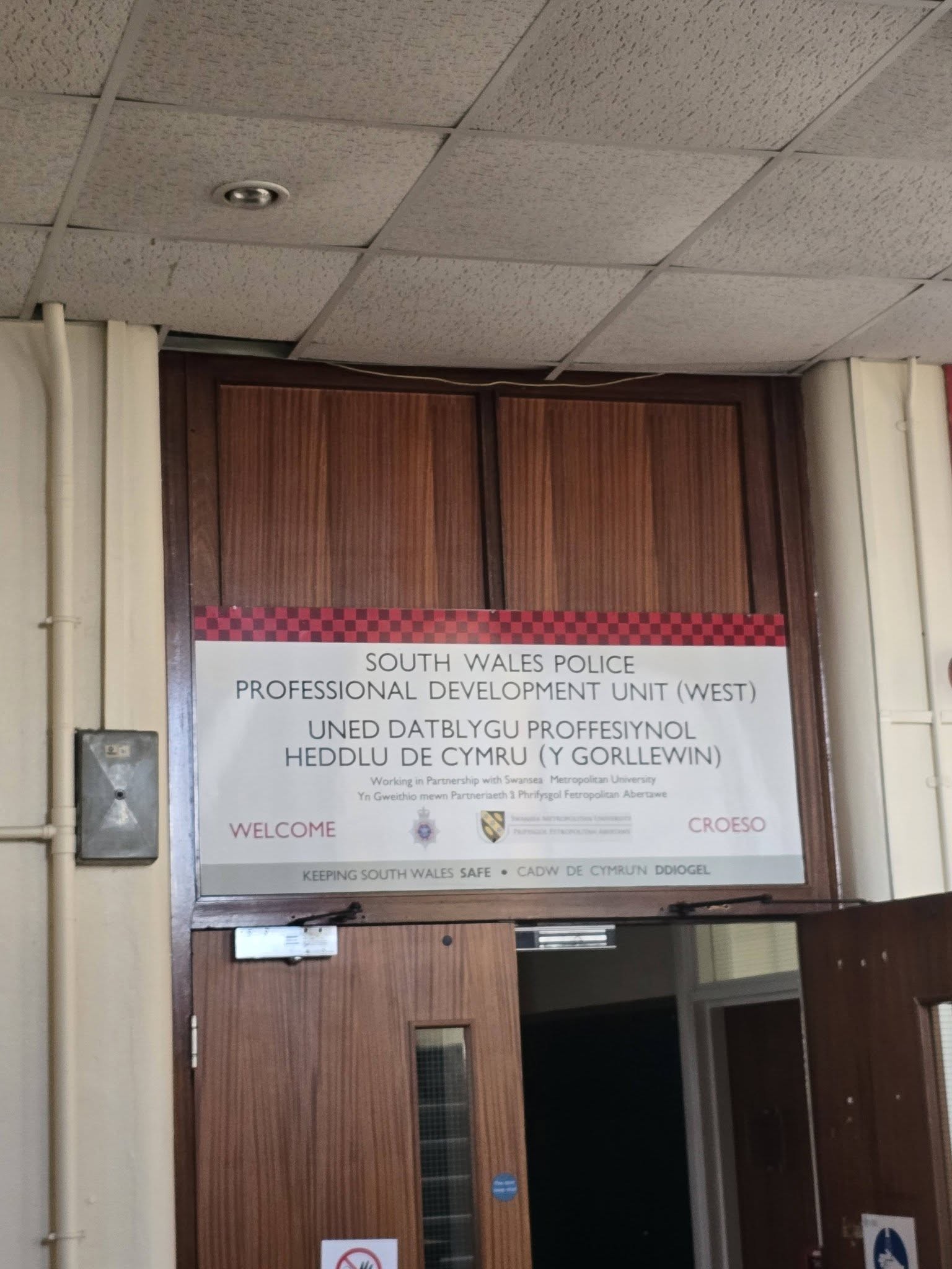 South Wales Police Professional Development Unit West bilingual welcome sign above wooden doors