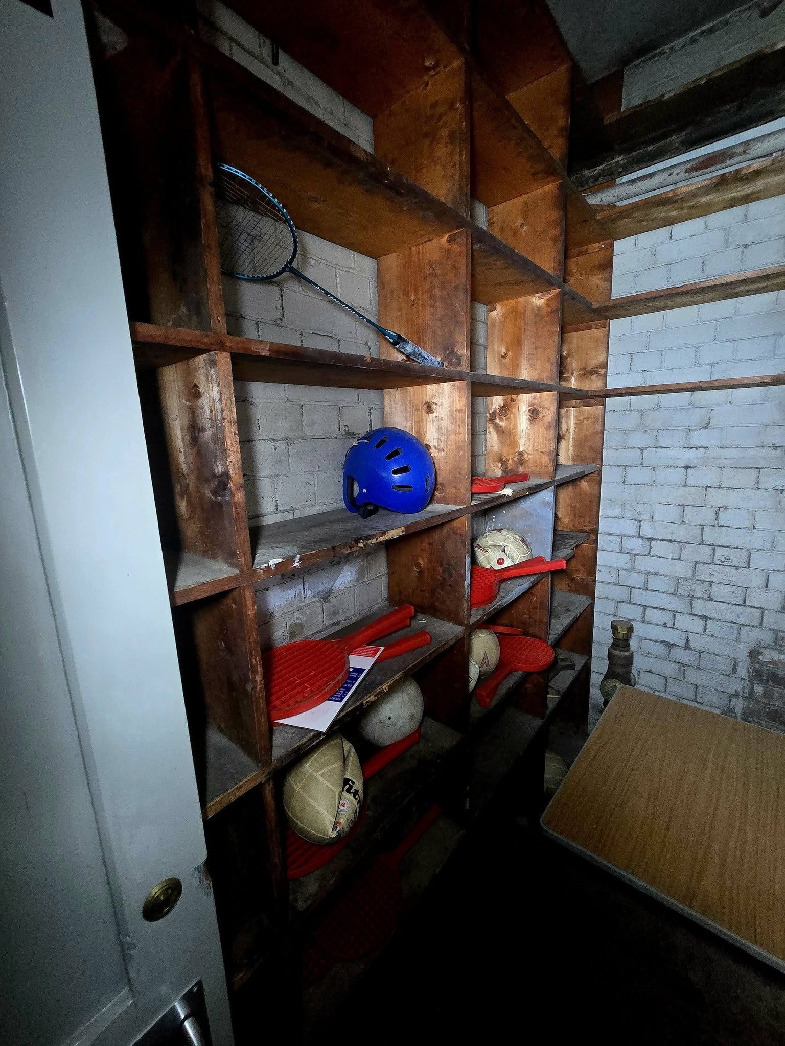 Wooden storage cupboard shelves holding old rackets balls and a blue helmet