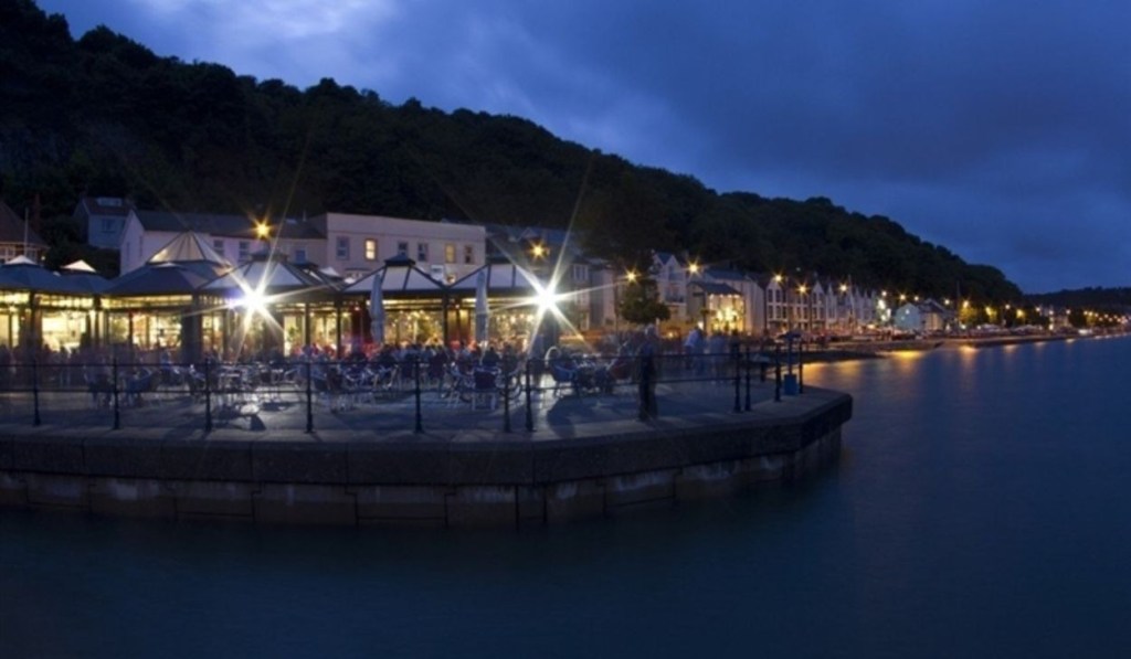 Verdi's cafe in Mumbles lit up at night, with diners at outdoor tables beside Swansea Bay