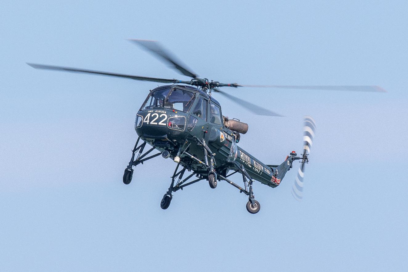 The Westland Wasp helicopter in dark Royal Navy livery marked HMS Aurora 422, in flight against a blue sky