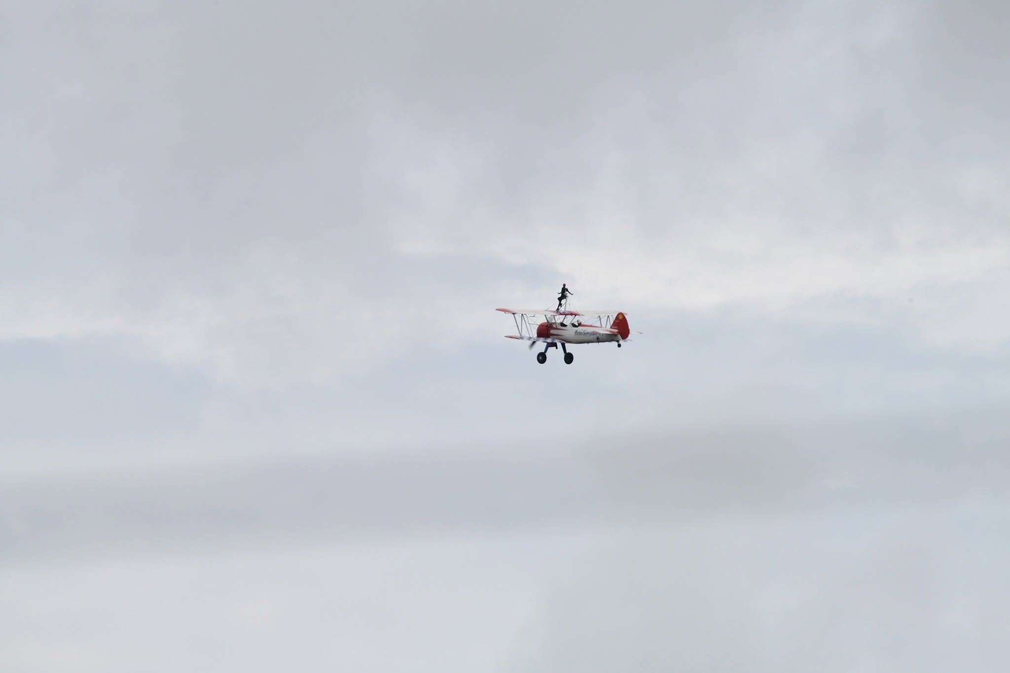 A red and white Stearman biplane with a wingwalker standing on the upper wing