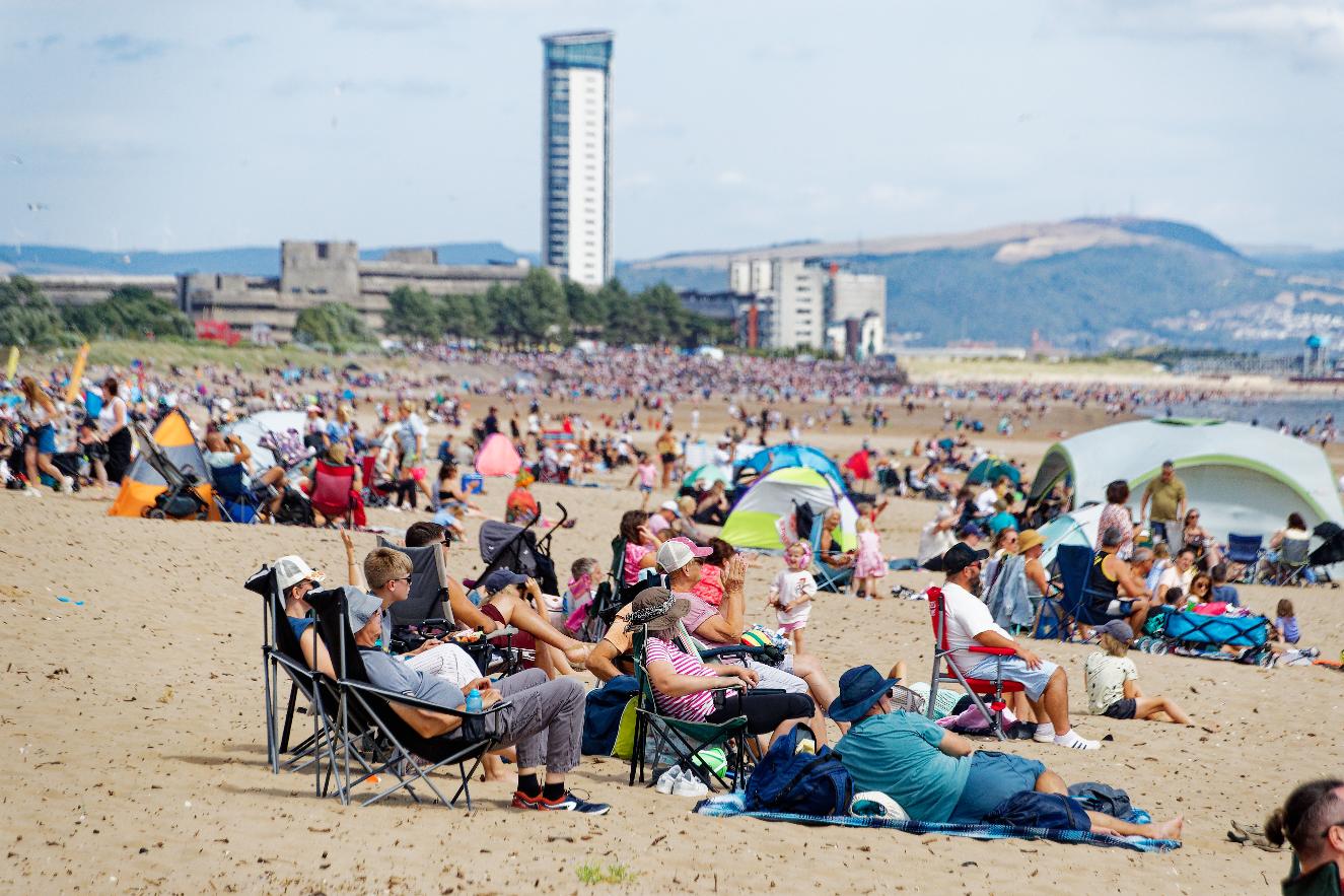 Crowds in deckchairs and tents packed along Swansea beach with the Meridian Tower and city behind
