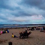 Drones spelling Nos Da above Goodnight over Swansea Bay, with crowds watching from the beach at dusk