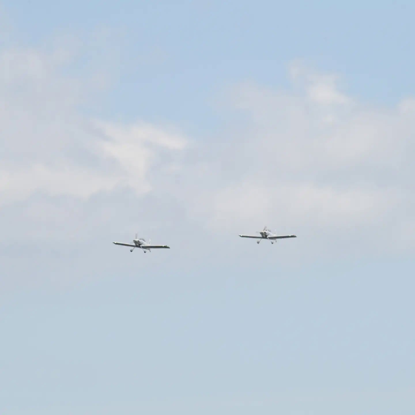 Two light aircraft flying wingtip to wingtip against a pale sky over Swansea Bay