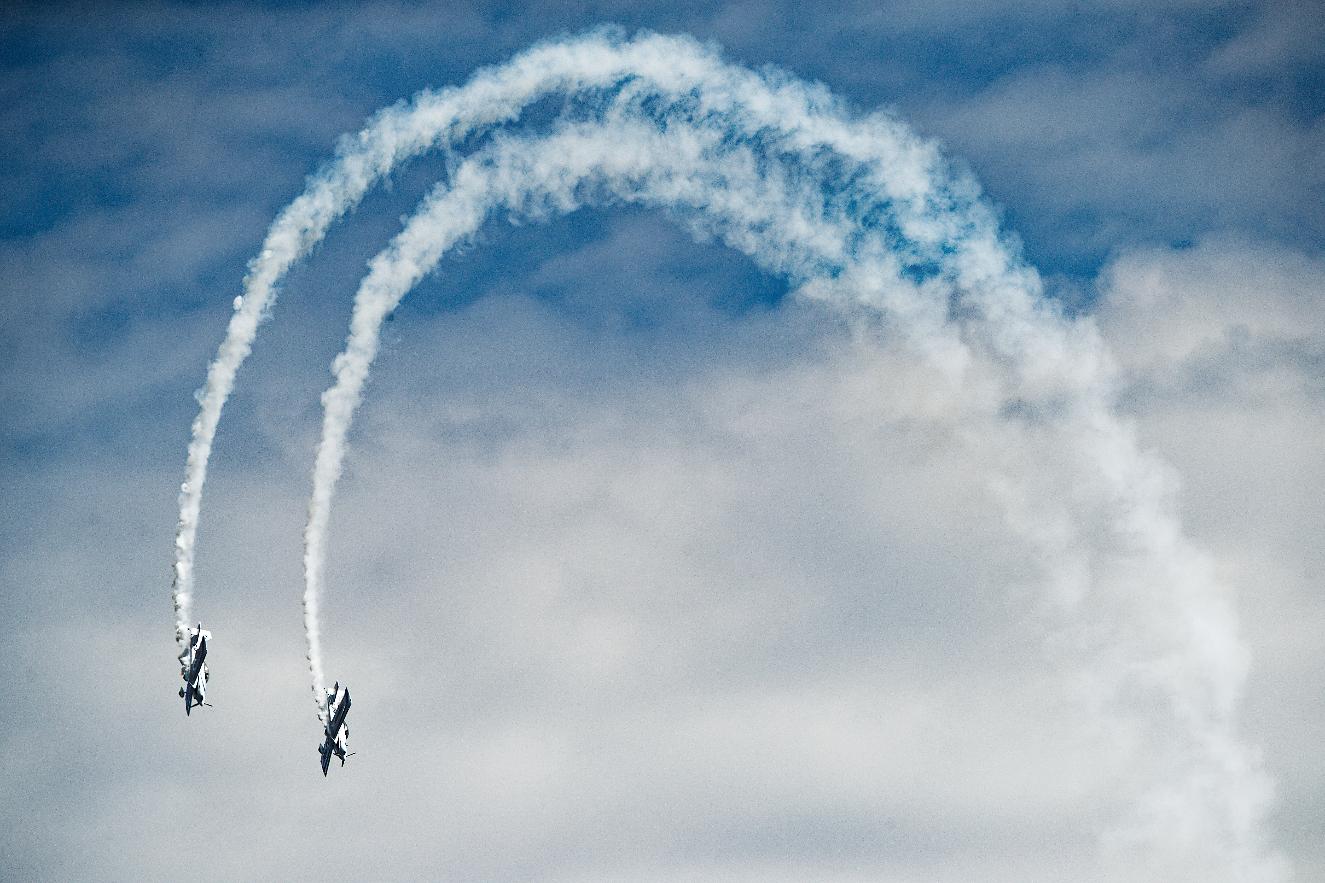 Two display aircraft descending together having drawn a wide arc of white smoke across a blue sky
