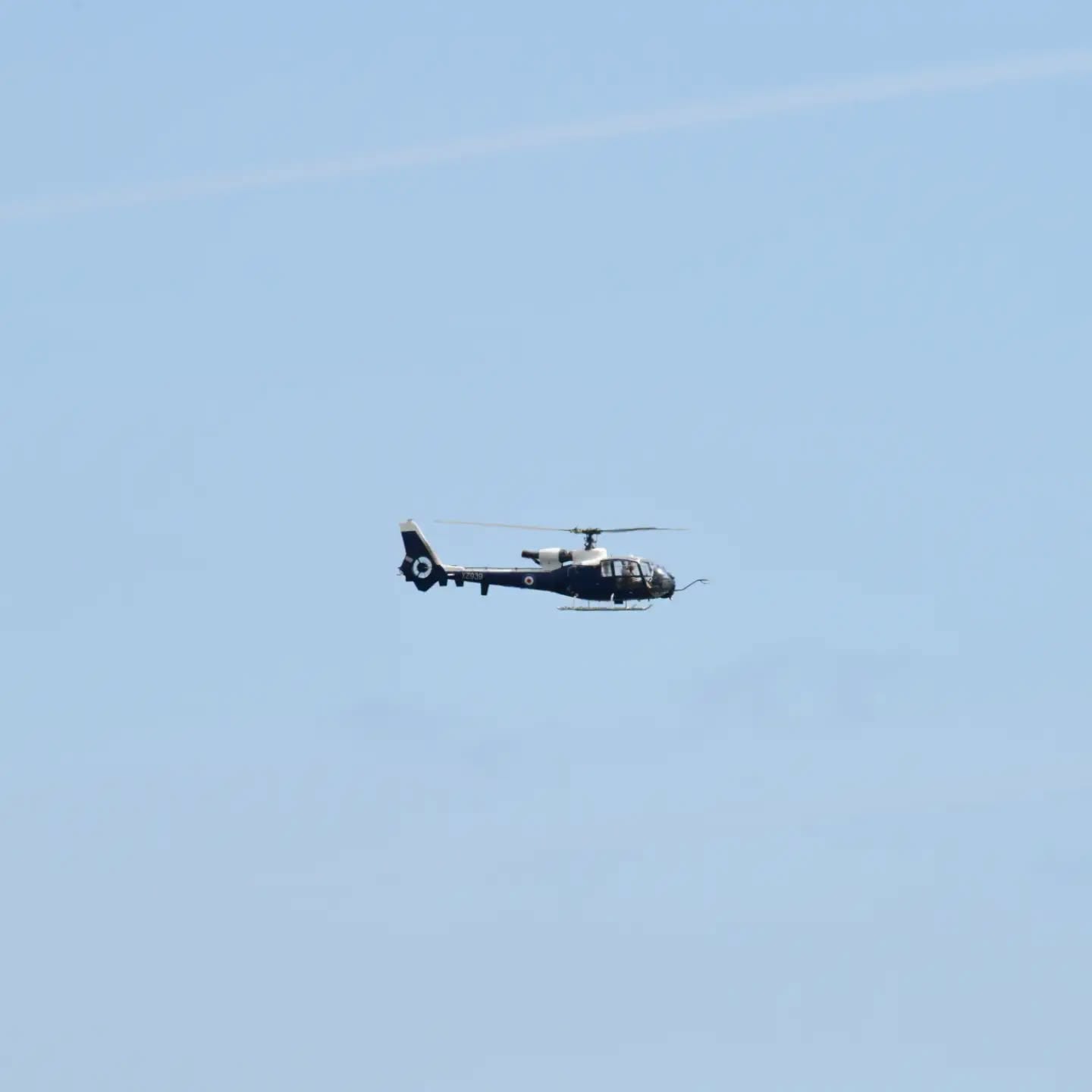 A dark blue Westland Gazelle helicopter in Royal Navy markings in flight over Swansea Bay