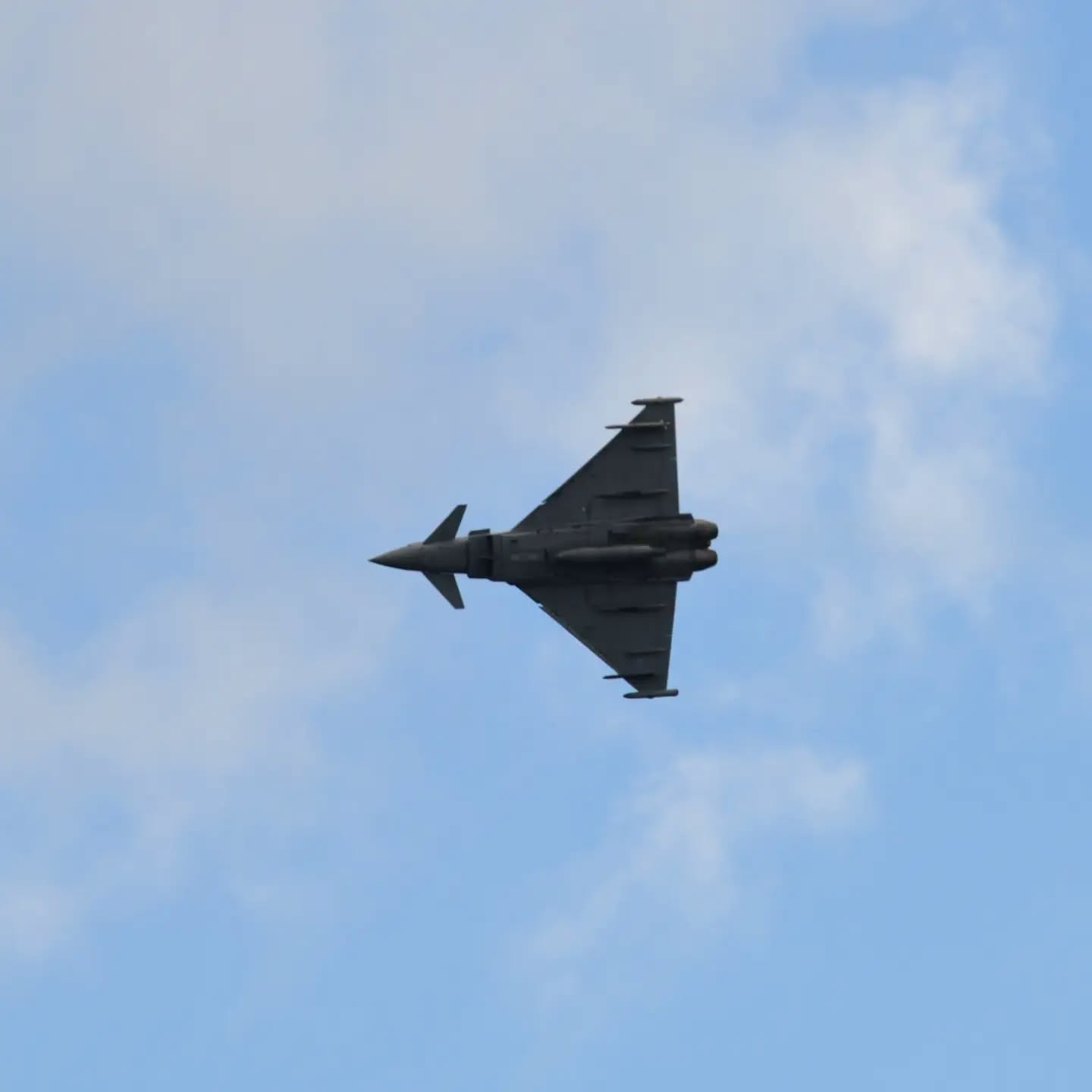 The underside of an RAF Typhoon fighter jet banking against cloud over Swansea Bay