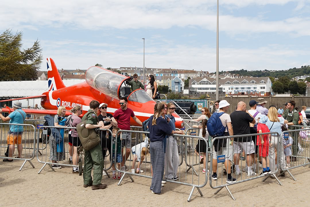 Crowds behind barriers around a red RAF Hawk jet parked on sand at Swansea seafront